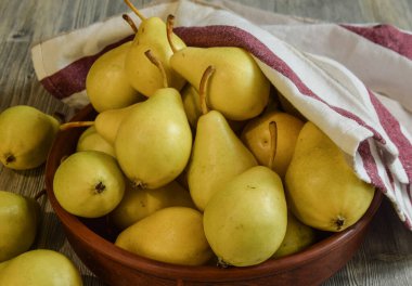 İçerideki ahşap masada kil kasede olgun sarı armutlar. Arka planda geleneksel bulaşık havlusu. Mevsim hasadı. Pişirmek için taze malzemeler. Yemeye hazır tatlı meyveler. Durgun hayat