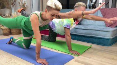 Tarz sahibi genç beyaz çift içeride spor minderleri üzerinde yoga dengesi egzersizi yapıyor. Orijinal dövmeleri olan pozitif bir kadın, yakışıklı erkek arkadaşı evde yoga esneme egzersizi yapıyor..