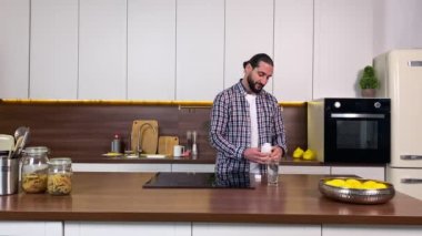 İçeride vitamin takviyesi alan pozitif sakallı yetişkin bir adam. Mutlu erkek kişi, ev mutfağında ilaç alarak ruh sağlığını korur. Evde beslenme ilaçlarıyla beslenen bir adam