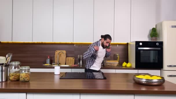 英俊的大胡子男人准备在家里的厨房急急忙忙地工作 时尚男工迟到了 他通过手机与老板交谈 喝咖啡 匆忙地在屋里穿衣 — 图库视频影像