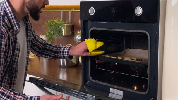 在家庭厨房使用烤箱进行积极的男性烹饪 快乐的丈夫戴着烤箱手套 打开炉灶 在平底锅上品尝食物 满意地打盹 男子在室内做饭 — 图库视频影像
