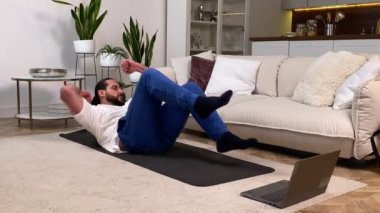 Evde Yetişkin Adam Antrenmanı. Atletik Erkek Diz-Dize Antrenman Yapıyor Laptop Bilgisayar 'da Çıtırdıyor İçerde Antrenman Yapıyor. Spor adam oturma odasında karın kaslarını kasıyor.