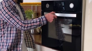 Handsome bearded man cooking baked vegetables at home. Househusband checking food in oven, smelling meal, enjoying delicious smell eating indoors. Positive guy doing household chores domestic kitchen
