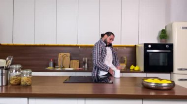 Scurrying mid adult man oversleeping getting ready for work in a hurry, talking phone boss or client at domestic kitchen. Handsome bearded male be late for appointment meeting. He in a rush at morning