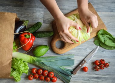 Top table view woman preparing healthy food order grocery shop indoors. Eco bag with pile of vegetables. Female hands peel fresh organic ingredients cutting board wooden table. Market to home shopping