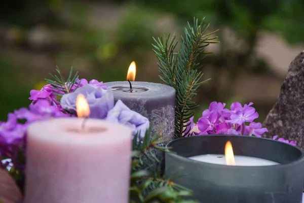Closeup burning candles purple flowers stone on blurred background. Selective focus on light candlewick. Beautiful composition with violet candles for spa treatment. Zen relax memorial concept.