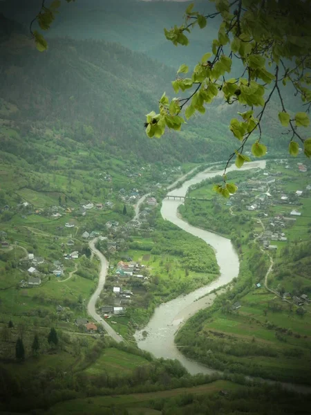Top view of valley of meandering river among small mountain village in foggy rainy day. Muddy water of mountain river while high water in highlands. View from hill. Rainy season