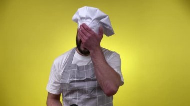 Sarı arka planda yanmış çörekleri göstermekten rahatsız olan, aşçı şapkalı, sakallı, boyalı genç adam şef. Hayal kırıklığına uğramış erkek aşçı, tatlı pişirmede başarısız olduğu için üzüntüsünü dile getiriyor.