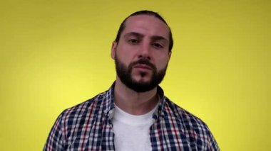 Ciddi yüz ifadesi olan yakışıklı sakallı adamın portresi kameraya bakıyor, soldan sağa dönüyor, izole edilmiş sarı arka plan üzerinde sıradan bir gömlek giyiyor. Erkek modelin basit doğal görünüşü.