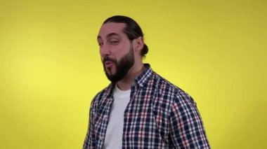 Resimli sakallı adam kamerayı işaret ediyor, göz kırpıyor, sarı arka planda izole edilmiş kameraya bakıyor. Oyuncak erkek giyimli, günlük kıyafetlerle flört eden, içerde kameraya parmak tabancalarını gösteren