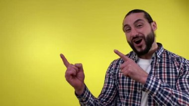 Pozitif sakallı adam, sarı arka planda izole edilmiş dişlek tebessümle kameraya bakarak, reklam için boş alana dikkatle bakıyor. Duyuru Reklam Kavramı