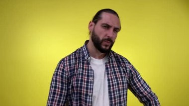 Kollarını kavuşturmuş yakışıklı sakallı adam, sarı arka planda izole edilmiş ciddi bir yüz ifadesiyle poz veriyor. İçerideki kameraya bakan katı erkek patron. İnsan duyguları yaşam tarzı konsepti