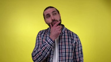 Sıradan giyinmiş yetişkin sakallı bir adam soru sormaktan endişeleniyor, endişeli, sarı arka planda el ele tutuşuyor. Çözüm arayan kafası karışmış orta yaşlı erkek, sorunu çöz