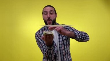Mutlu orta yaşlı sakallı adam kameraya para atıyor, banknotları saçıyor, şans piyangosunu kutluyor, para karıyla övünüyor. İzole edilmiş sarı arka plan çekimleri. Konsepti yakmak için para