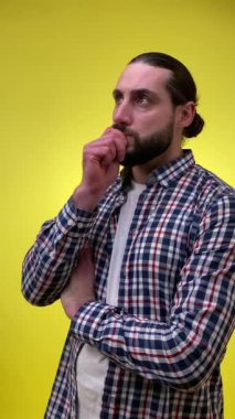 Dikey çekimde, yetişkin sakallı bir adam gündelik kıyafetleri hakkında endişeli, endişeli, sarı arka planda el ele tutuşmuş. Çözüm arayan kafası karışmış orta yaşlı erkek, sorunu çöz