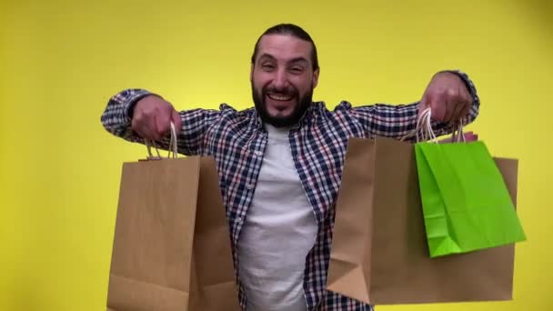 愉快的中年男子购物 欣赏新的购物展示与商场精品店购买的购物袋 手持包装孤立地站在黄色背景 消费主义概念 — 图库视频影像