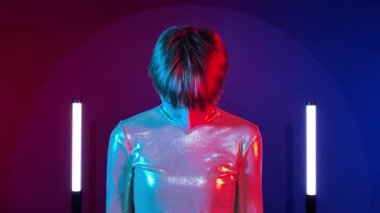 Dişi android robot, sentetik tebessümle kapalı alanda aydınlanıyor. Yapay zeka konsepti, bilim kurgu, gelecek. Fütürist ışıltılı kostüm giymiş genç bir kadın. Renkli ışıklandırma.