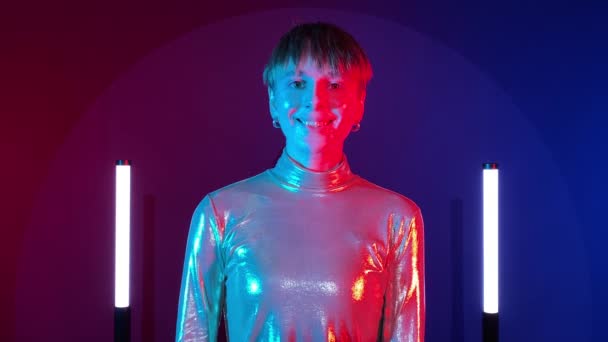 女性机器人机器人会做出合成的微笑 学会在室内用霓虹灯照明来表达喜悦 Ai概念 年轻的成年女子在未来灿烂的服装艺术五彩缤纷照明 — 图库视频影像