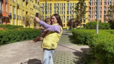 Selfie çeken neşeli genç bir kadın küçük köpeği açık havada tutuyor. Evcil hayvan konsepti. Ev hayvanlarının fotoğraflarını kullanan sevimli bir kadın ebeveyn halka açık parkta güneşli bir günde kaynaşmaktan zevk alıyor.