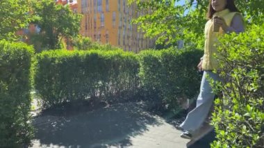 Parlak güneş ışığında parkta tasmayla dolaşan güzel bir genç bayan köpek. Şehir köpeği konsepti, şehir yaşam tarzı. Arka planda yerleşim bölgesinin renkli binaları var. Kızlar açık havada kahve içer.