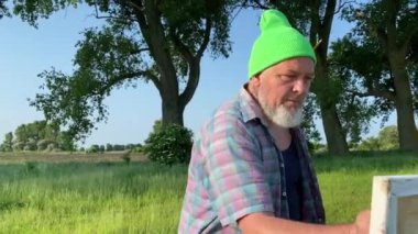 Orta yaşlı ressam sabah güneşinde boya fırçasıyla yağlı boya resim yapar. Hevesli sanatçı adam çayırdaki tuvale hazırlanıyor. Manzara görünümü, arkaplanda ufuk çizgisi