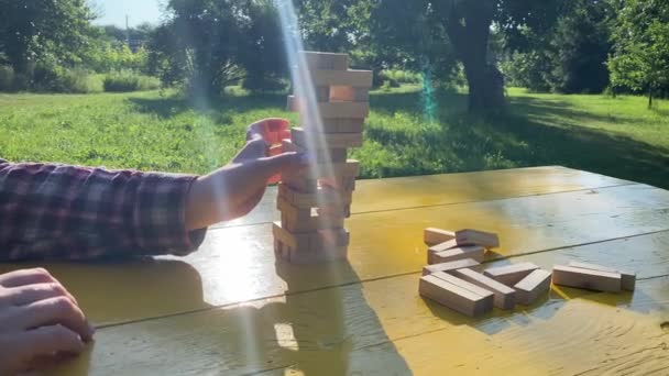 認識できない女性は日の出に黄色のテーブルの屋外でブロック除去ゲームをプレイします バランスの概念 女性の手は人生の決定のアナロジーとしてブロックを取るためのより簡単な方法を見つける 背景の景観公園 — ストック動画