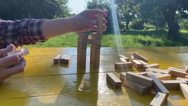 平衡概念 成年妇女在日出时用木块在室外的黄色桌子上建造塔楼 一个平衡生活的类比 背景为金光闪闪的美丽的绿色自然景观公园 — 图库视频影像
