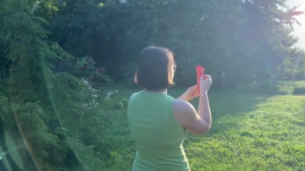 平衡概念 在日出时分 后视镜成年女子在美丽的园林中 在明亮的阳光下发射纸飞机 黄金时刻 宁静的女性使用折纸来表达平衡状态 — 图库视频影像