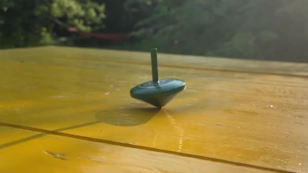 特写单纺纱顶部绿色旋转在黄色的桌子上 而其他顶部玩具落在室外 旋转物体作为平衡生活的类比 美丽的风景公园金色的阳光背景 — 图库视频影像