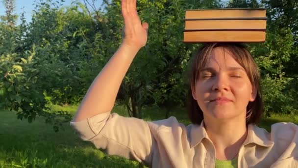 Fiatal Felnőtt Könyveket Egyensúlyozik Fejen Csukott Szemmel Szabadban Napnyugtakor Egyensúlykoncepció — Stock videók