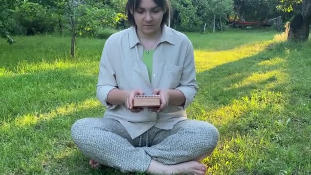 迷人的年轻成年女子在日出时在户外演奏小乐器 平衡概念 女性放松冥想创作简朴的音乐 坐在金黄的阳光下的绿色园林 — 图库视频影像