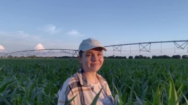 Çekici genç kadın çiftçi ya da tarımcı başını çevirir, kameraya bakar, altın saat günbatımında gülümser. Temiz gökyüzünün arka planında tarım sulama ekipmanları. Tarım sektörü kavramı, meslek