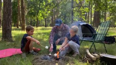 Harika bir aile kamp gezisi. Babalar ve çocuklar kamp ateşinin etrafında toplanıp güneşli bir günde açık havada tahta çubuklarda marshmallow kızartırlar. Ormanda yürüyüş yaparken dışarıda yemek pişirmek.