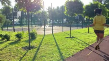 Coşkulu, çok ırklı bir genç kadın sabah sporunda çevre düzenlemesi yapılan parka gidiyor. İp atlayarak sınırsız enerji aşımı yapıyor. Açık mavi gökyüzü ve altın güneş ışığı. Etkin yaşam biçimi