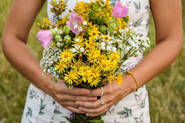 Orta kesimdeki çok ırklı genç bir kadın, pitoresk bir çayırda bir buket kır çiçeği tutuyor. Huzurlu sahne, onun doğanın güzelliği ve dışarıdaki huzurlu anları ile olan bağlantısını yakalar.