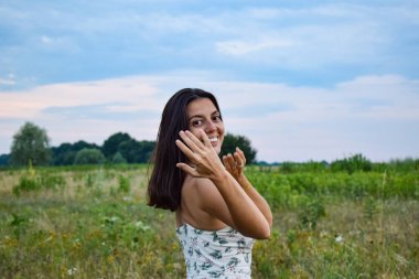 Çok ırklı genç bir kadının portresi alacakaranlıktaki pitoresk çayır zeminine pozitiflik neşe saçıyor. Yüzü coşkulu duyguları yansıtıyor. Sahnenin büyüleyici atmosferini mükemmel bir şekilde eşleştiriyor.