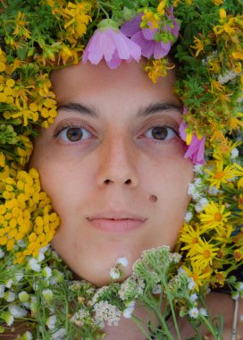 Kameraya bakan dingin, çok ırklı genç bir kadının yakın plan portresi. Yüzü canlı bir çiçek dizisiyle süslenmişti. Resmedilmeye değer çayır bitkileriyle.