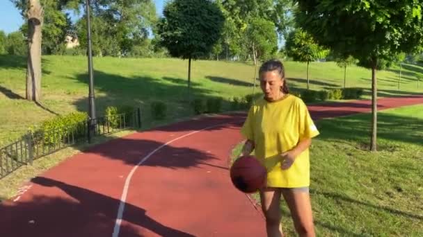バスケットボールのスキルを持つ多種多様な若い女性は デイブレイク時に公共の公園でポーズします 女性スポーツ選手は自信を持って指のバウンスボールにバスケットボールを回します 背景のスポーツ会場裁判所 — ストック動画
