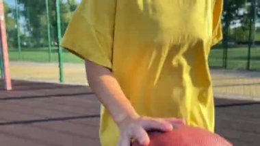 Enerjik, çok ırklı genç bir kadın güneşli bir sabahta halk parkında tutkulu bir şekilde basketbol topu sürüyor. Becerikli bir şekilde topu potaya doğru atıyor. Rekabetin keyfi ve aktif uğraşlar