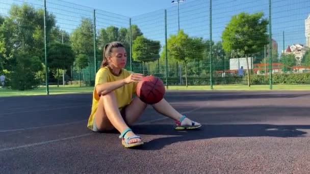Πολυφυλετική Νεαρή Γυναίκα Κάθεται Μια Μπάλα Μπάσκετ Απολαμβάνοντας Τον Πρωινό — Αρχείο Βίντεο