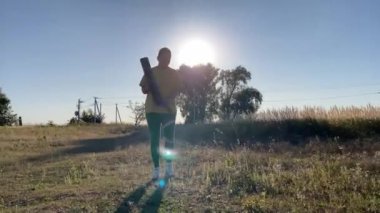 Hareketli spor kıyafetleri içindeki kararlı genç kadın sakin bir kırsal kesimde akşam antrenmanına hazırlanıyor. Açık mavi gökyüzü, altın akşam güneş ışığı vurgusu pozitifliği, gücü