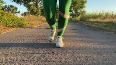Gün batımında kırsal bir yolda koşan, kırsal bölgenin altın saatinde parlayan genç bir kadın. Spor ayakkabılarındaki ritmik hareketler koşunun enerjisini yakalıyor.