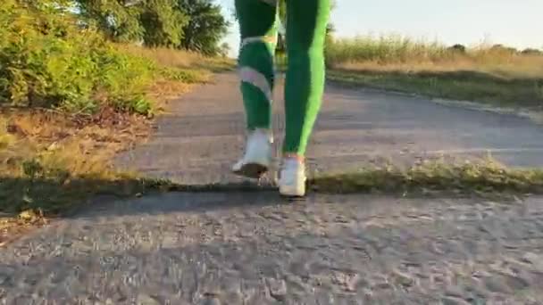 低いセクションの若い女性は日没で田舎の道路をジョギングし 田舎の自然の風景の黄金の時間の光を浴びます ランのエネルギー献身をキャプチャするスポーツシューズのリズミックムムーブメント足 — ストック動画
