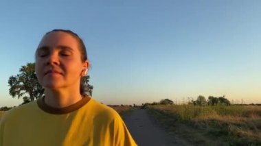 Genç bir kadın, büyüleyici altın saat günbatımında pitoresk bir kır yolunda akşam koşusu yapıyor. Geniş bir fotokopi alanı olan bir portre, açık havada yaptığı koşunun sükunetini yansıtıyor.