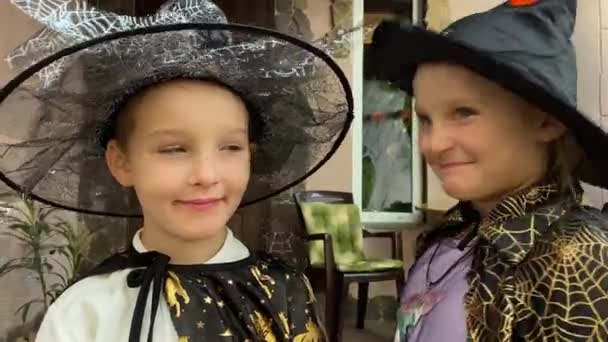 ハロウィーンの魅力的な子供たちの肖像画 ハロウィーンのお祝いの衣装 カメラを見て 魔女の帽子を着て 不気味な装飾 コブウェブ カボチャのジャック ランタンで装飾されたフロントポーチに立って — ストック動画