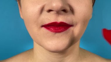 Tanınmayan genç bir kadın canlı renkte dudaklarını Chili biberini ısırıyor ve içerideki baharatlı yemeğin tadını çıkarıyor. Kırmızı ruj, mavi arka planda izole edilmiş acı biberi yer.