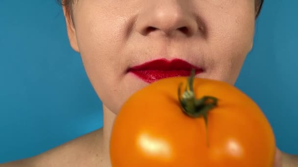 难以辨认的年轻女子的嘴唇生动地着色 咬着黄色的西红柿 品尝着室内多汁蔬菜的味道 特写口红口红口红吃素食隔离在蓝色背景下 — 图库视频影像