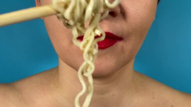 Tanımlanamayan genç bir kadın canlı renkli dudaklar yemek çubuklarıyla erişte yiyor, içeride lezzetli öğle yemekleri yiyor. Kapalı ağız kırmızı ruj. Makarnanın tadını çıkartıyor. Ya da mavi arka planda ramen.