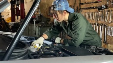 Tulumlu genç bir kadın bir araba bakım istasyonunda çalışıyor. Kapalı alanda teknik bakım yapıyor. Kadın tamirci motor yağını değiştiriyor, yağ dolgusu boynuna huni sokuyor. Arkaplanda araçlar
