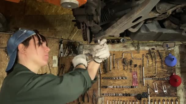 穿着工作服的年轻妇女在汽车加油站工作 进行汽车维修 用套筒扳手拧紧底盘紧固件 熟练的女机修工修理吊车 — 图库视频影像
